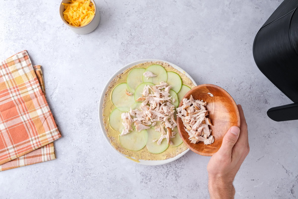 hand pouring bowl of shredded turkey into tortilla with countertop around.
