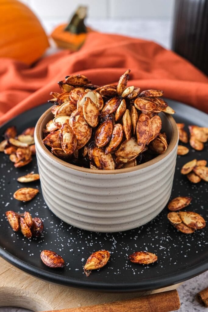 small bowl of crispy pumpkin seeds on black plate.