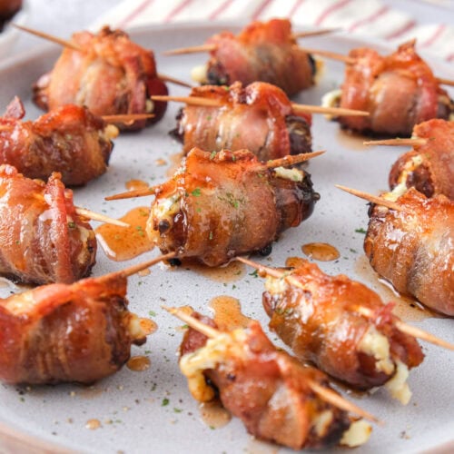 bacon wrapped stuffed dates on a plate with toothpicks in them.