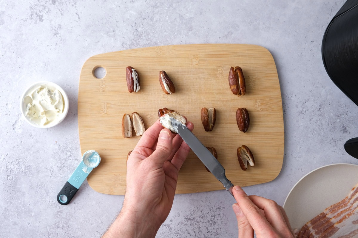 hand spreading cream cheese into dates with cutting board underneath.