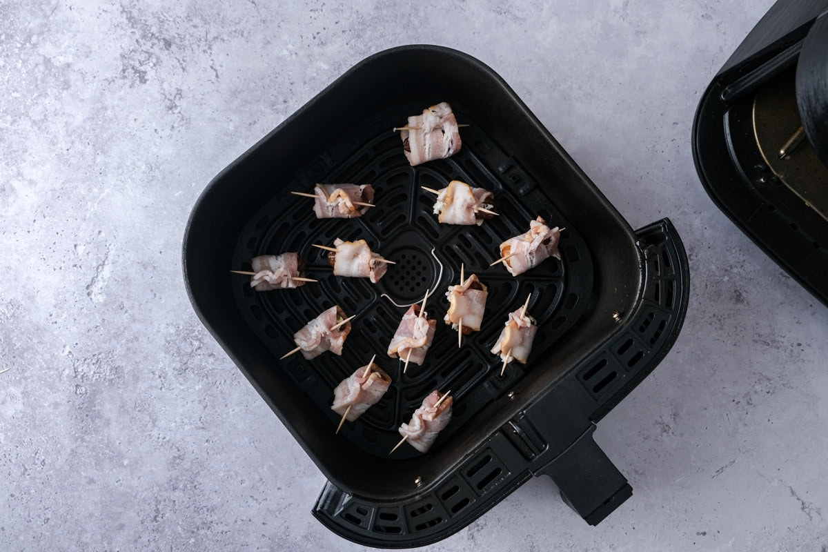 bacon wrapped dates arranged in air fryer basket on counter.