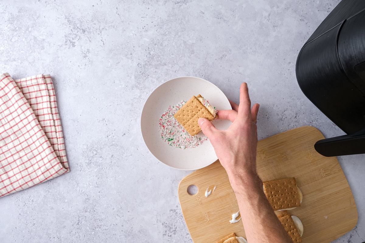hand dipping smores into crushed candy cane in bowl on counter.