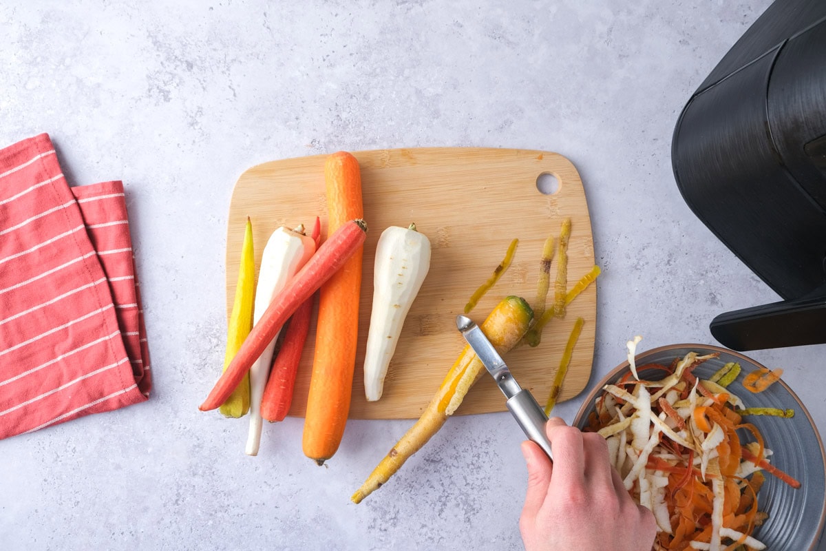 hand peeling root vegetables on counter with cutting board underneath.