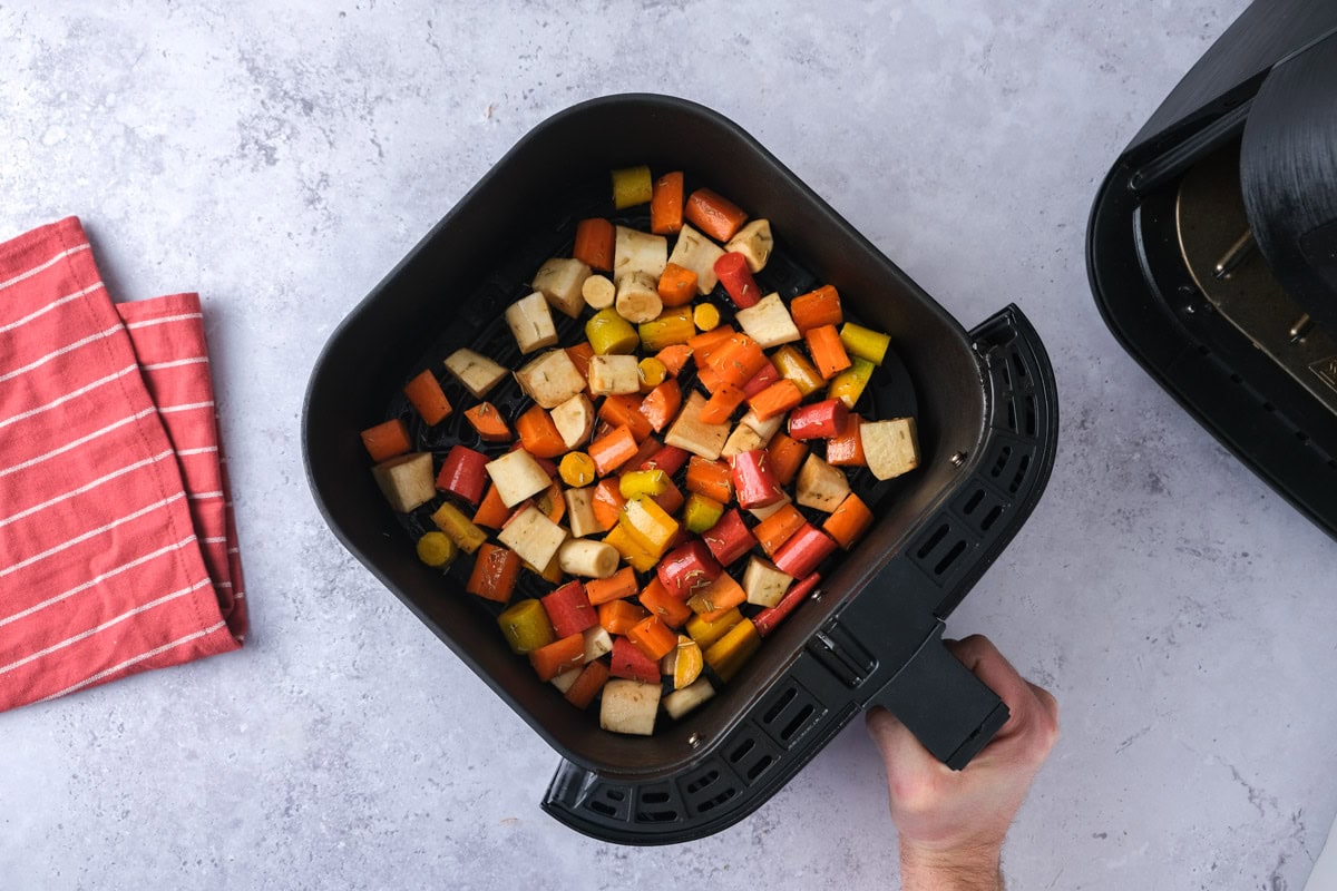 raw root vegetables in air fryer basket with counter around.