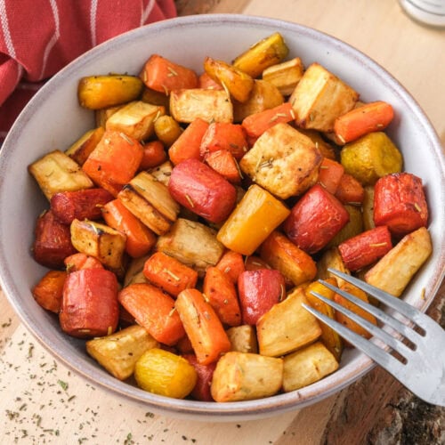 bowl of cooked root vegetables sitting on wooden board.