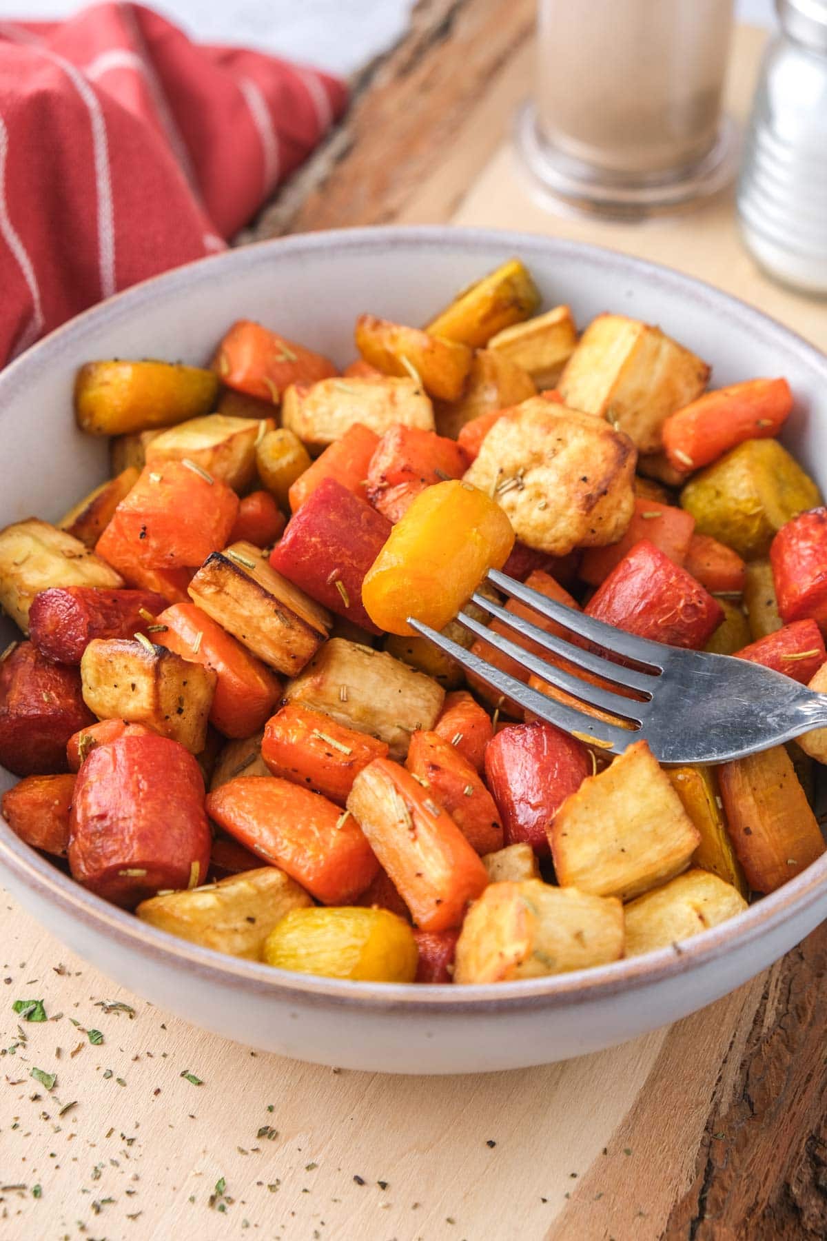 bowl of cooked root vegetables on wooden board with fork in bowl.
