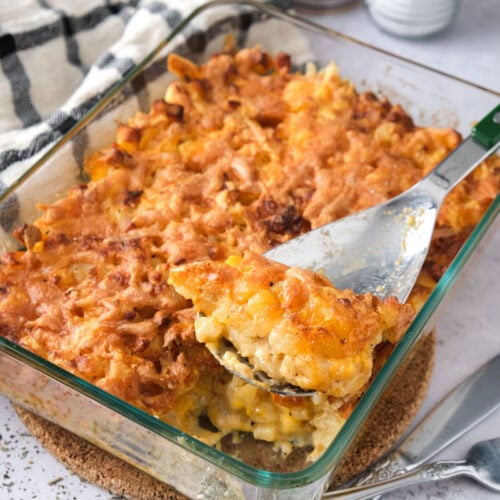 cheese and potato bake in glass dish with green and silver serving spoon sticking out.