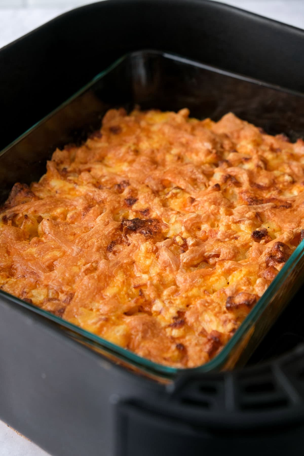 crispy cheese potato bake in glass dish sitting in air fryer basket.