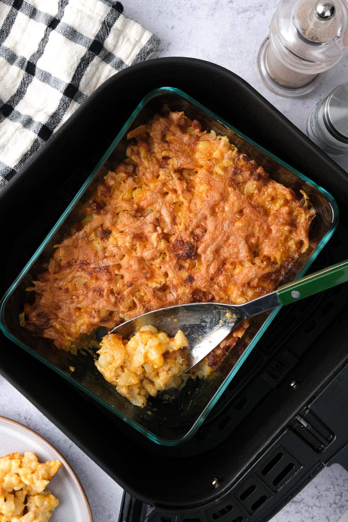 serving spoon with cheese potato bake on it serving out of air fryer basket.
