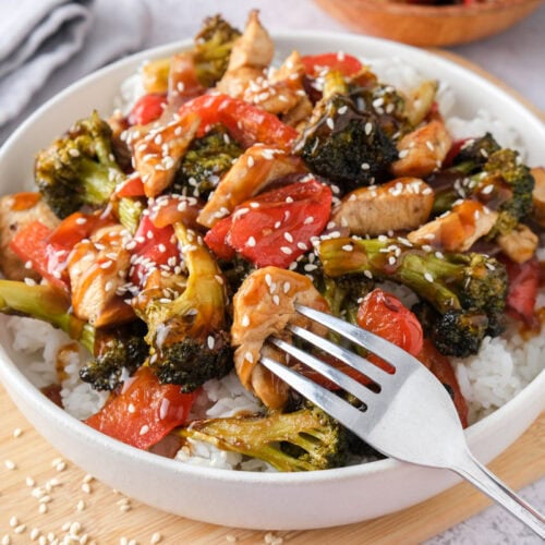 bowl of chicken and vegetables covered in sauce with fork piercing chicken.