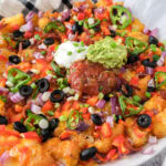 loaded tater tots on parchment paper with salsa and sour cream on top.