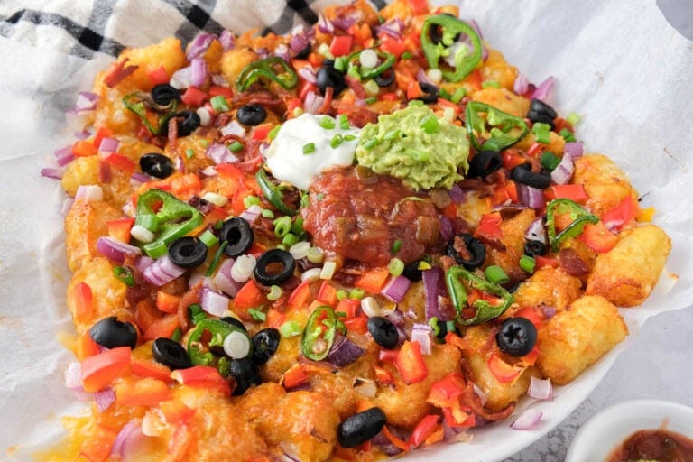 loaded tater tots on parchment paper with salsa and sour cream on top.