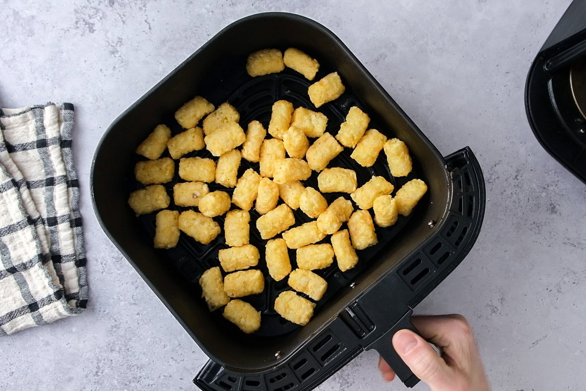 frozen tater tots in black air fryer basket on counter.