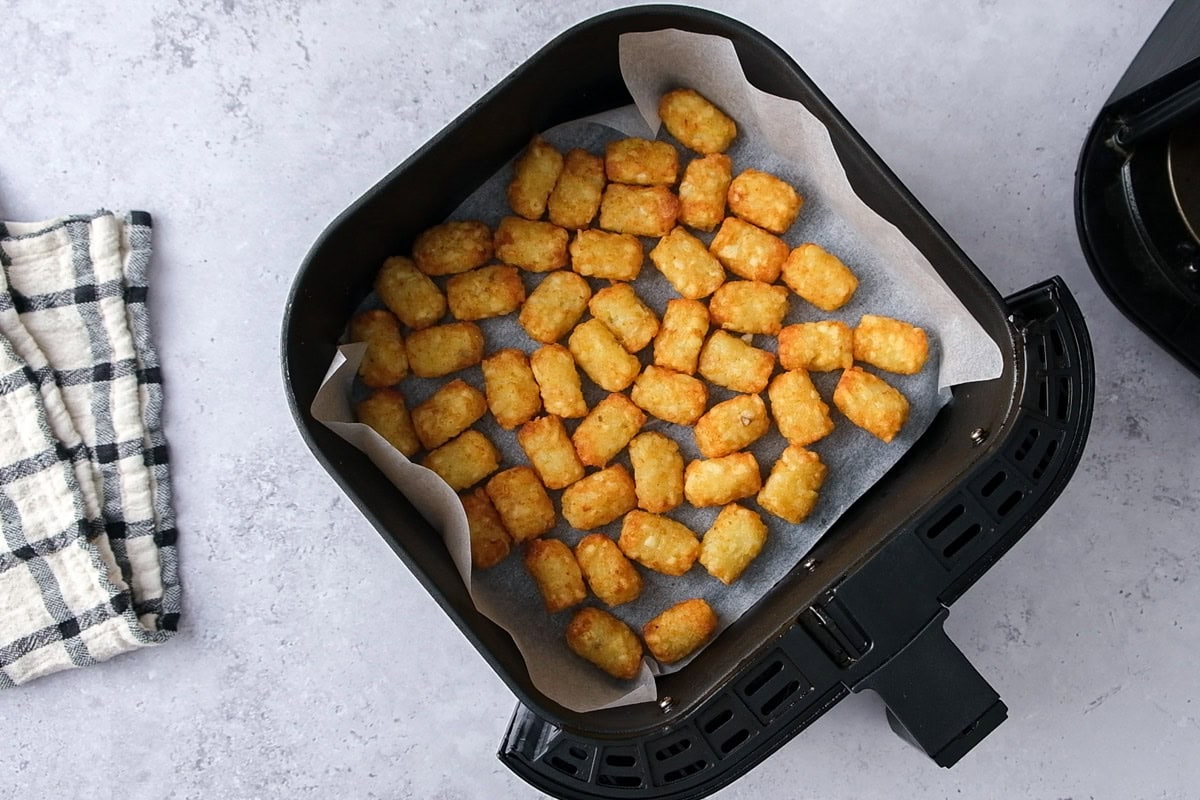 crispy cooked tater tots on parchment paper in air fryer basket.