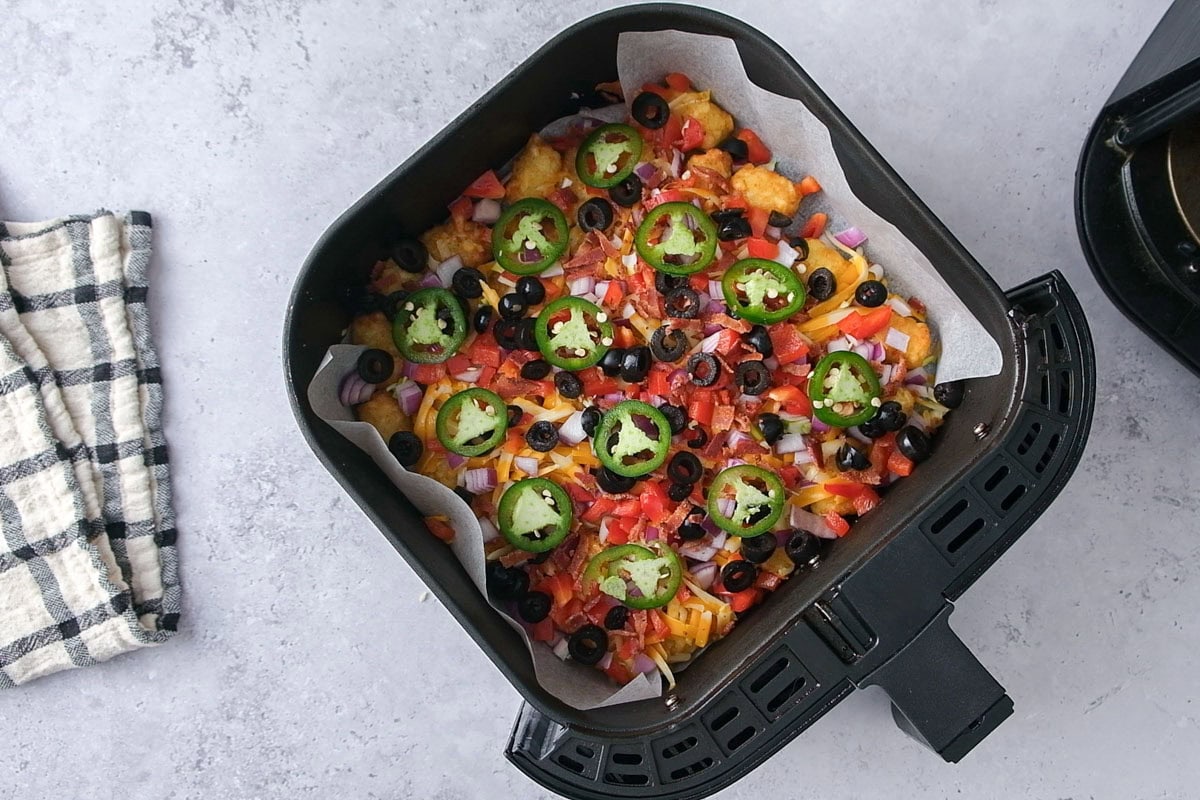 tater tots in air fryer loaded with toppings.