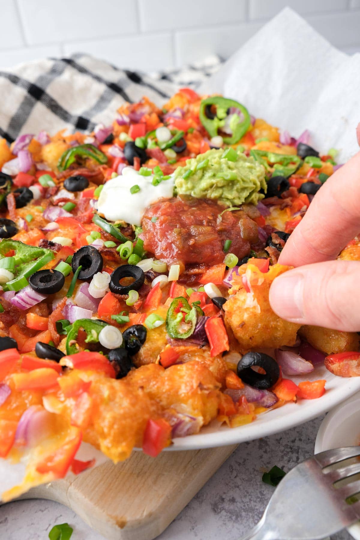 hand grabbing tater tot from loaded taters tots on plate.