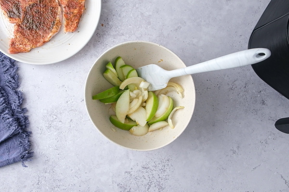 bowl of apples and onions with seasonings being mixed with a spatula.