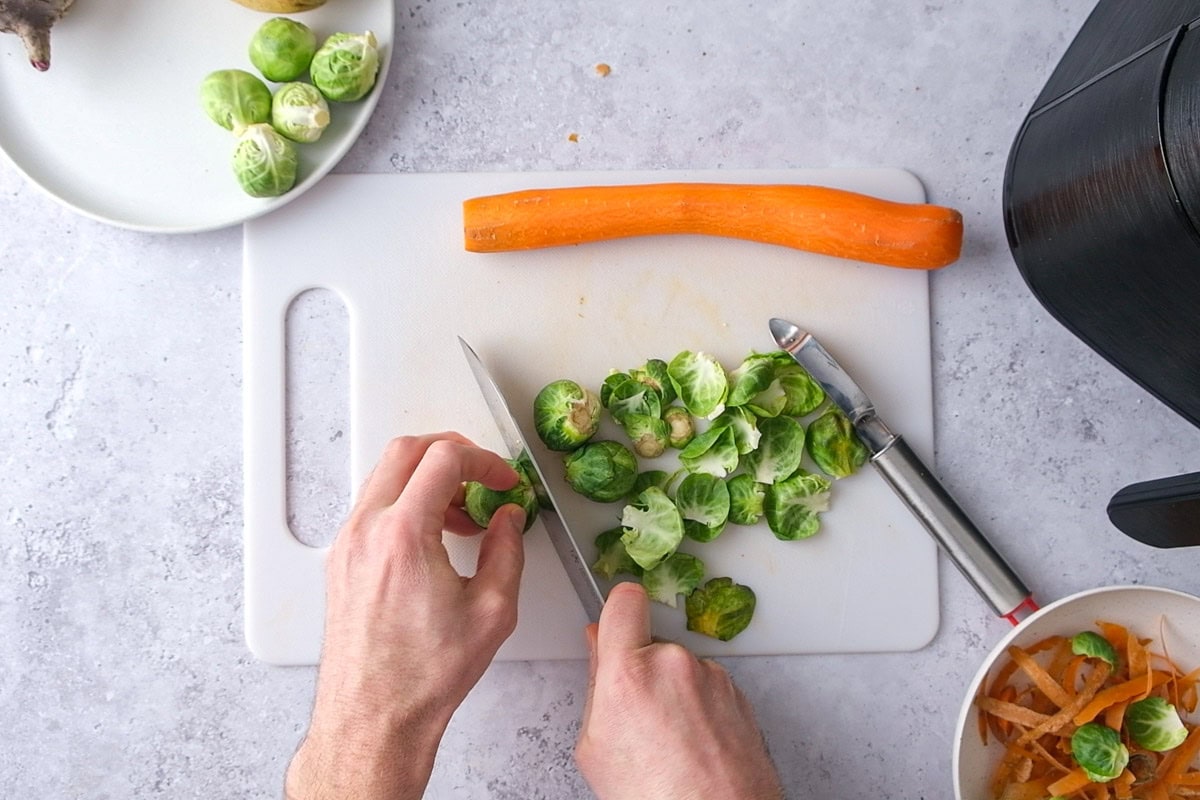 hand trimming brussels sprouts on white cutting board on counter.