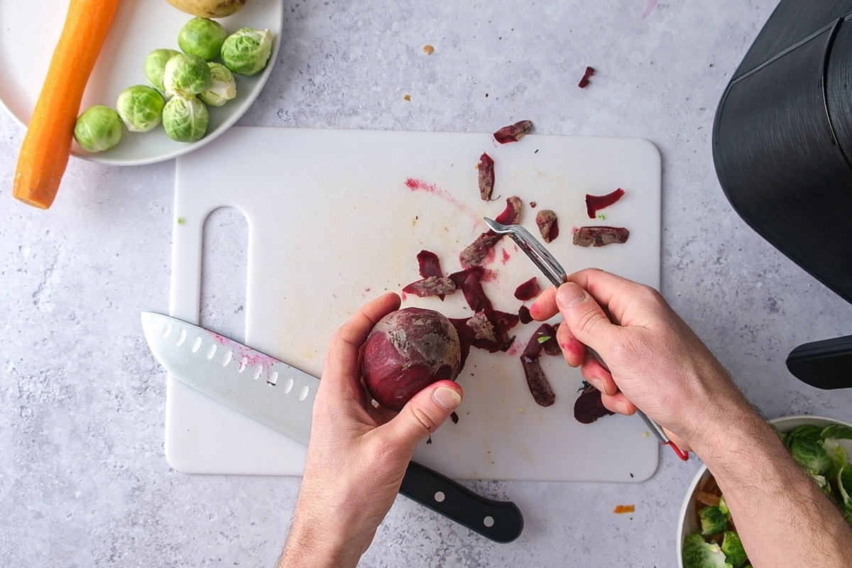 beet peels on cutting board beside hand peeling a whole beet.