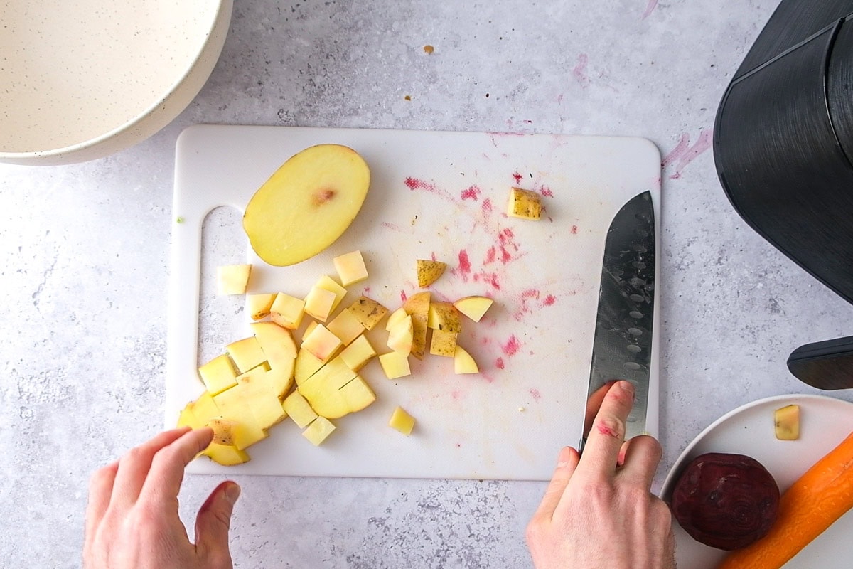 hand with large knife cutting yellow potato on white cutting board on counter.