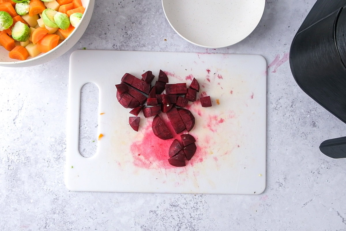 raw beets cut into cubes on white cutting board with bowls beside.