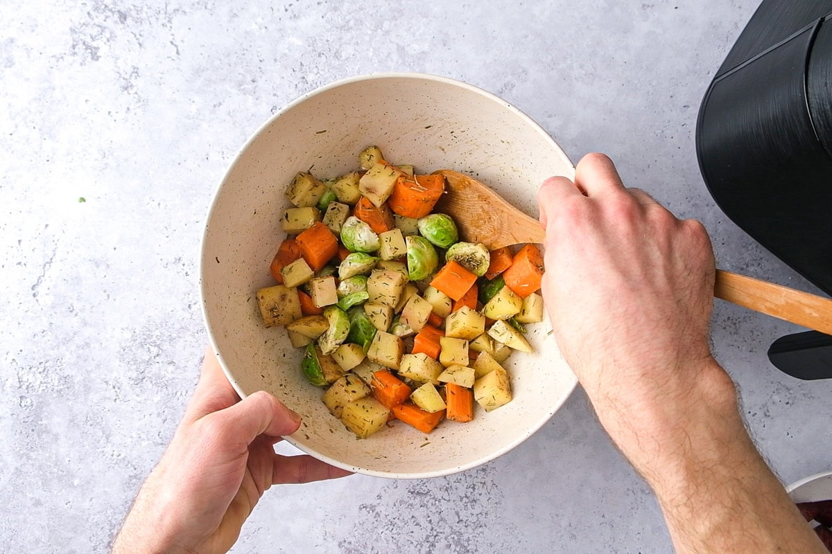 hand holding wooden spoon mixing cut vegetables in a large bowl.