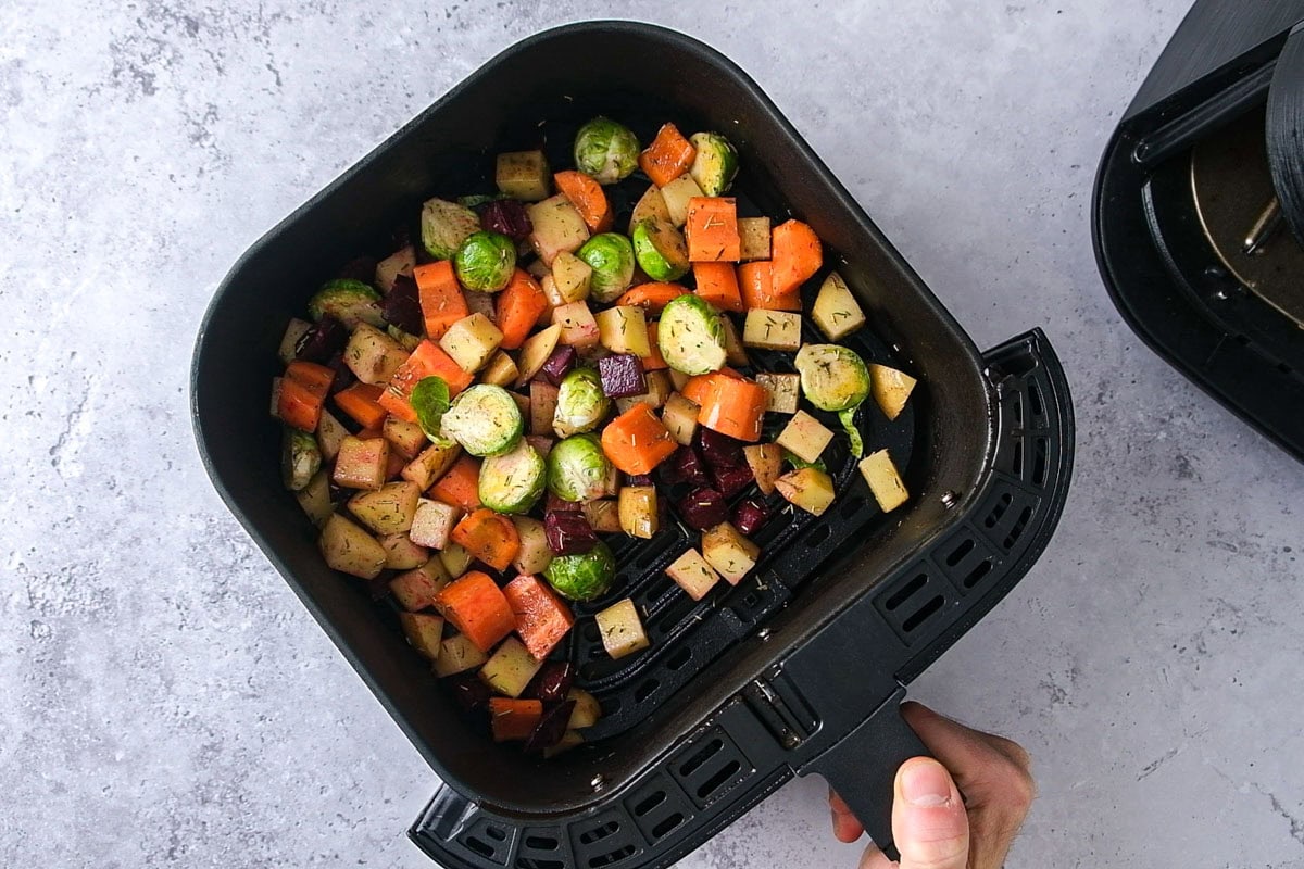 hand shaking air fryer basket filled with raw vegetables.