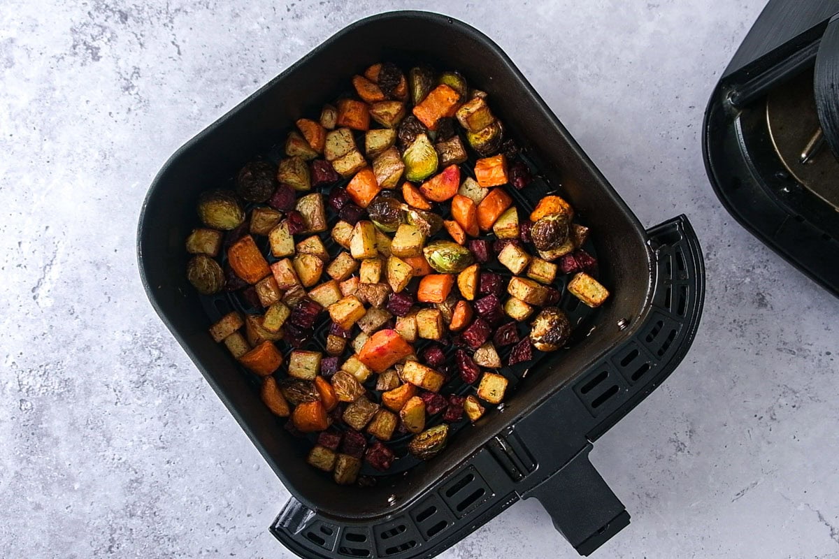 cooked winter vegetables in black air fryer basket with counter around.