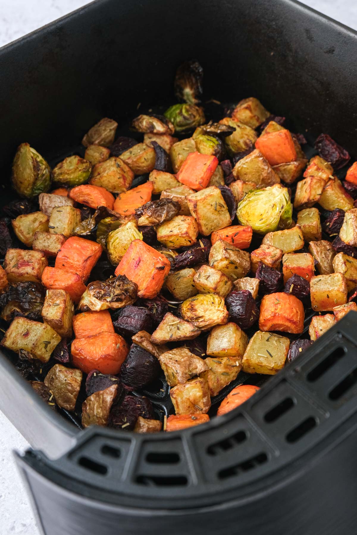roasted vegetables in black air fryer basket.