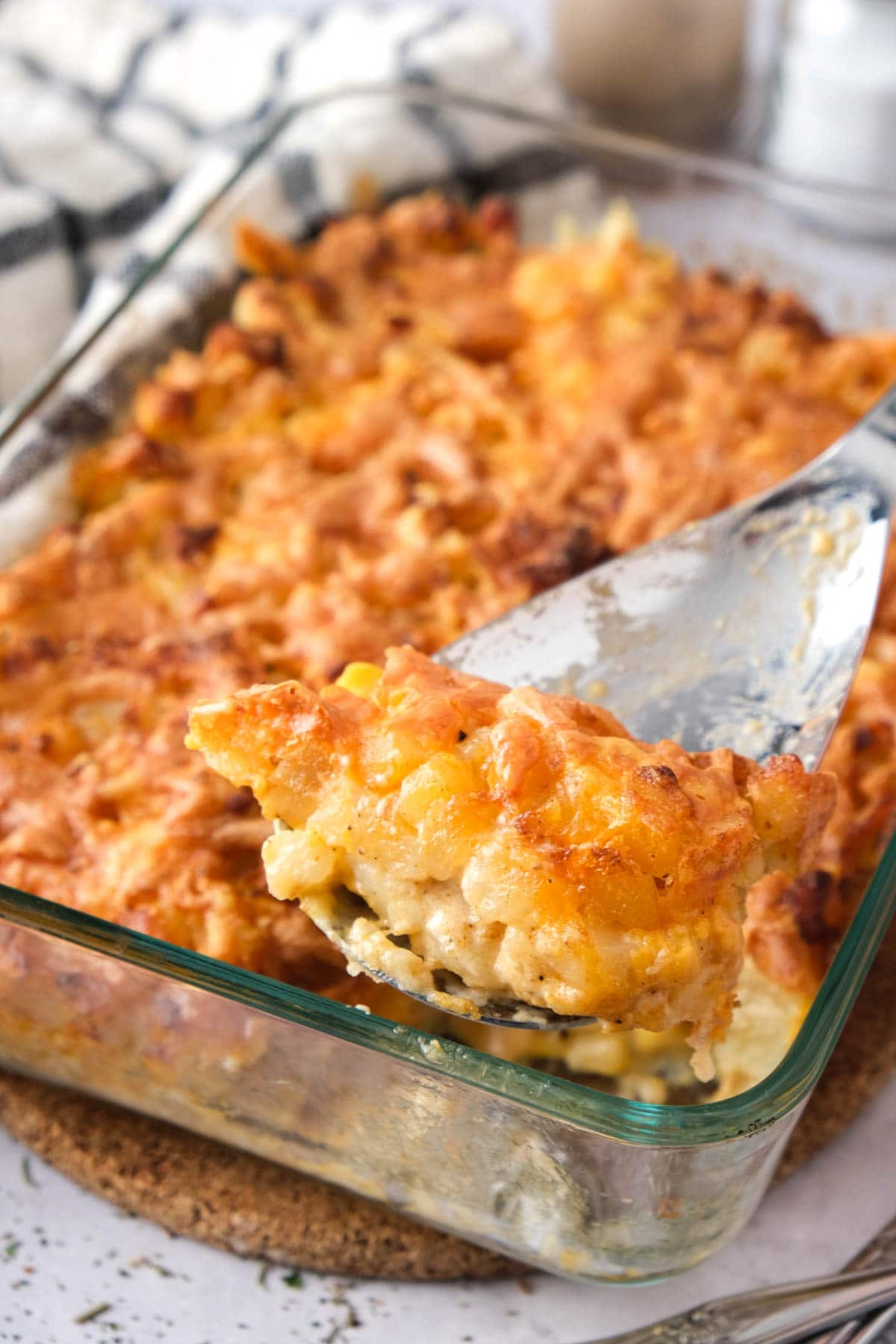 cheese and potato bake in glass dish on counter with serving spoon lifting some out.