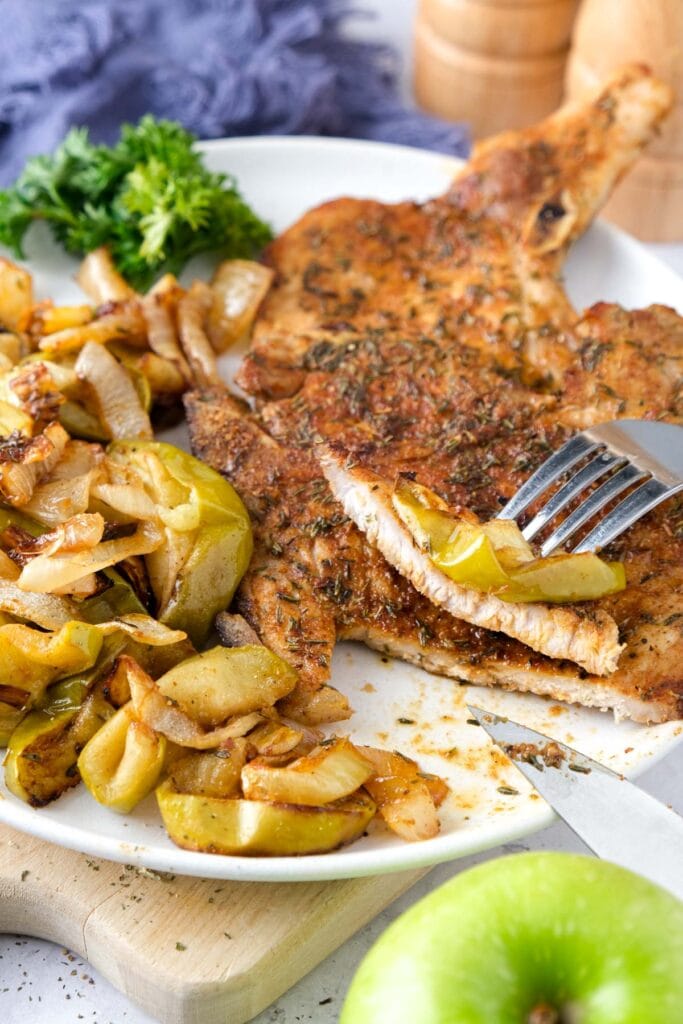 plate of cooked pork chops and apples with cloth and salt shakers behind.