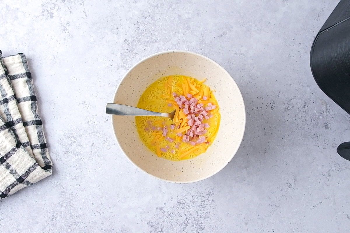 mixing bowl of egg cheese and diced ham with fork sticking out.