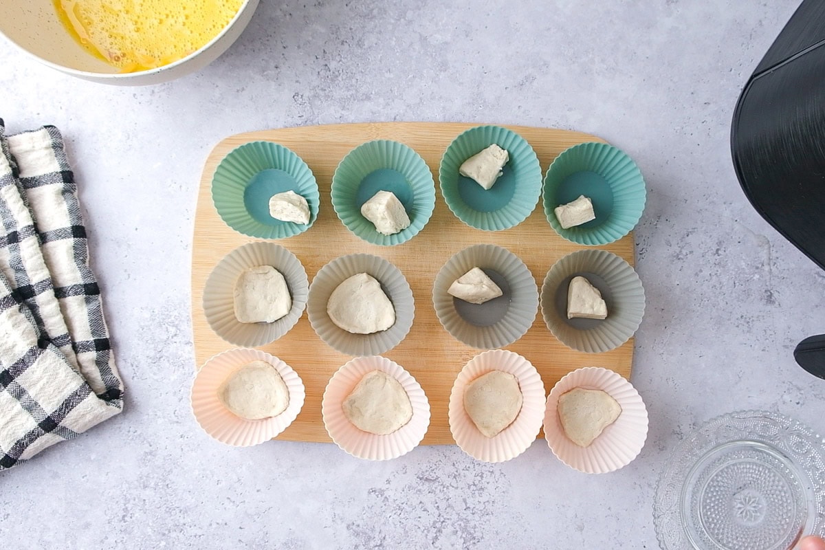 pieces of raw biscuit dough in silicone muffin cups on counter.