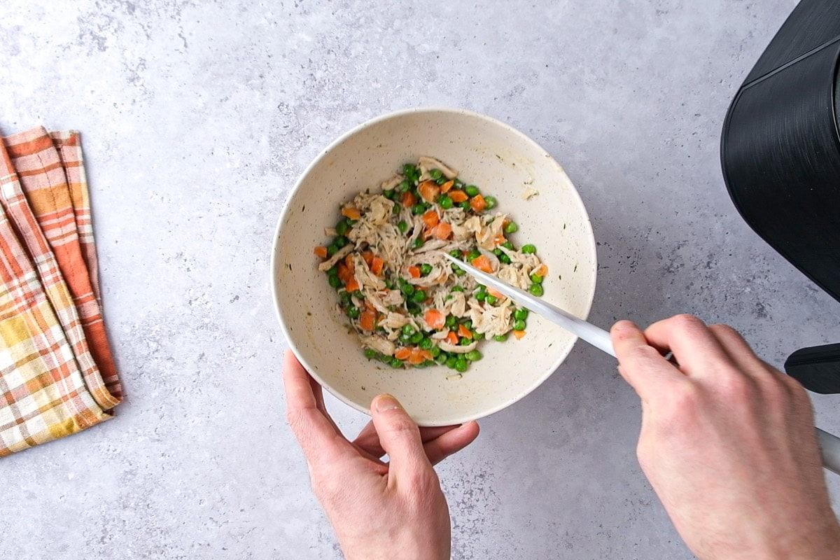 hand mixing vegetables and broth in bowl on counter.