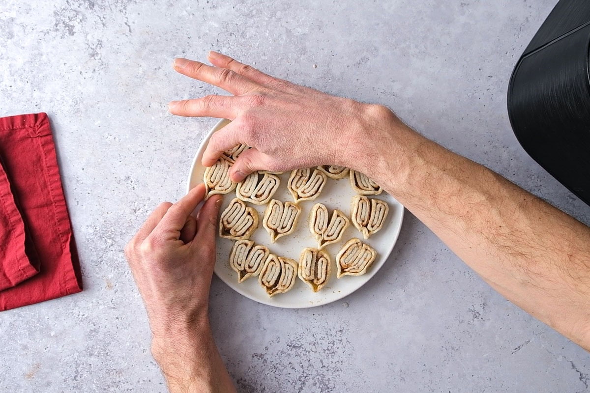 hand holding and pinching puff pastry pieces on a plate.