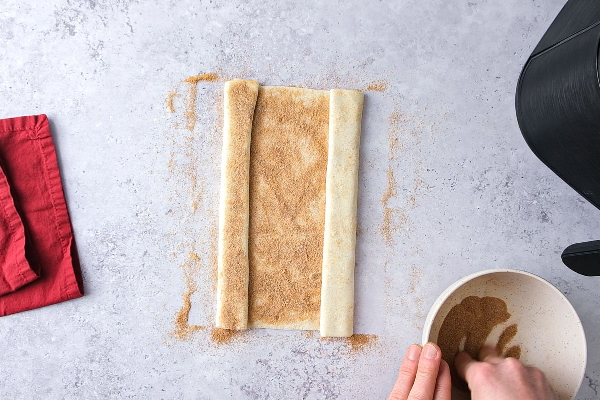puff pastry folded on counter covered in cinnamon and sugar.