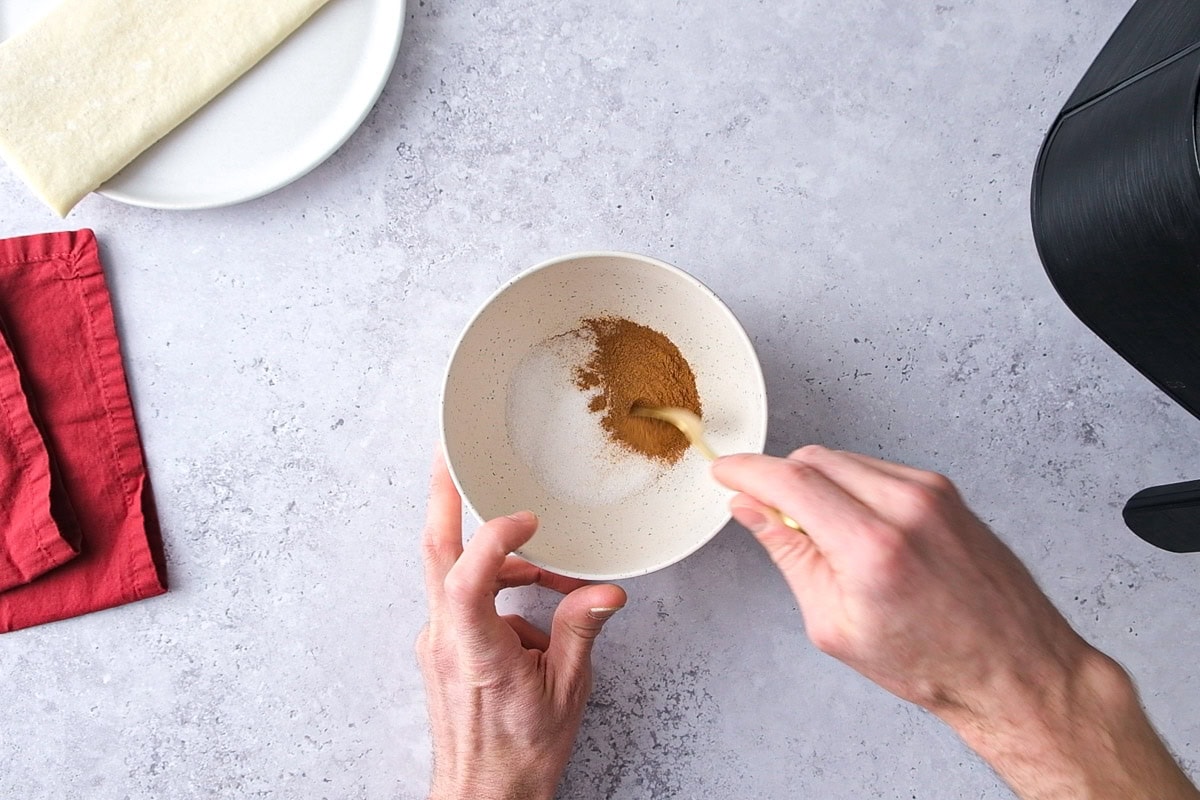hand mixing cinnamon and sugar in bowl on counter.