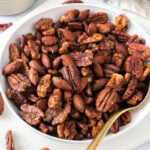 sweet and spicy nuts in white bowl with golden spoon sticking out.