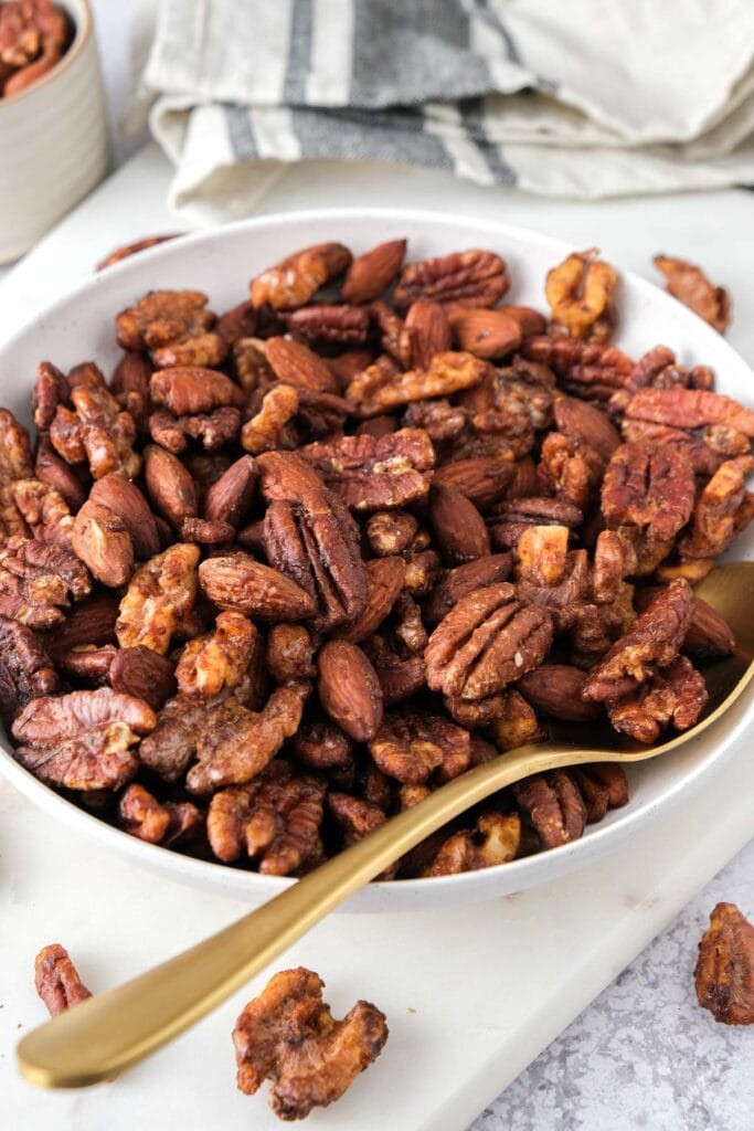 bowl of sweet and spicy mixed nuts on counter with serving spoon in the bowl.