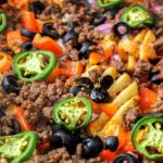 photo of Irish nachos with waffle fries, jalapeno, olives, and more in black air fryer with text overlay "air fryer Irish nachos".