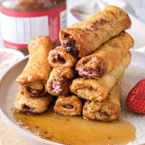 french toast roll ups on plate with berries and syrup.