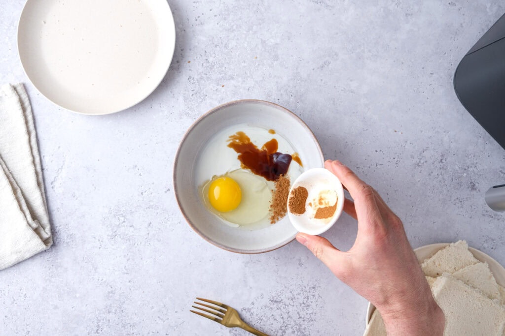 hand pouring cinnamon into bowl of egg and other ingredients.