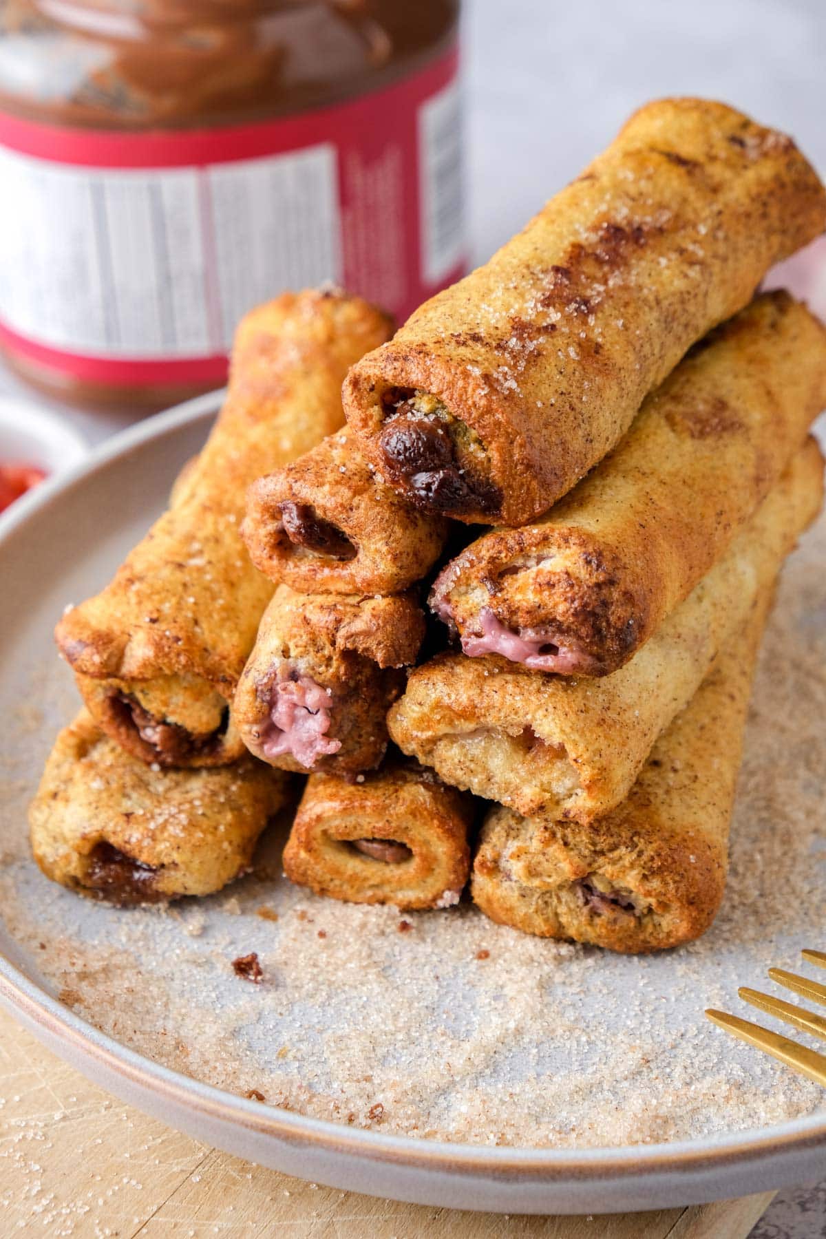 french toast roll ups stacked on a plate with cinnamon and sugar around them.