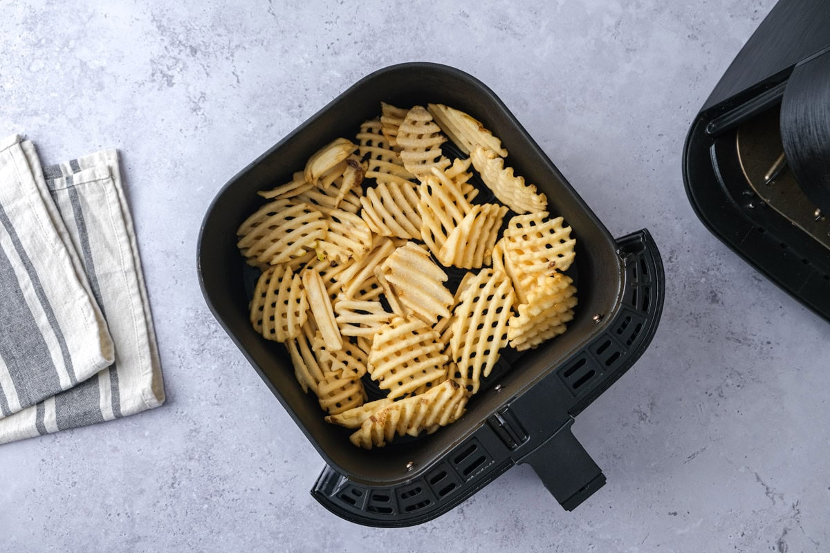 frozen waffle fries in air fryer basket on counter top.
