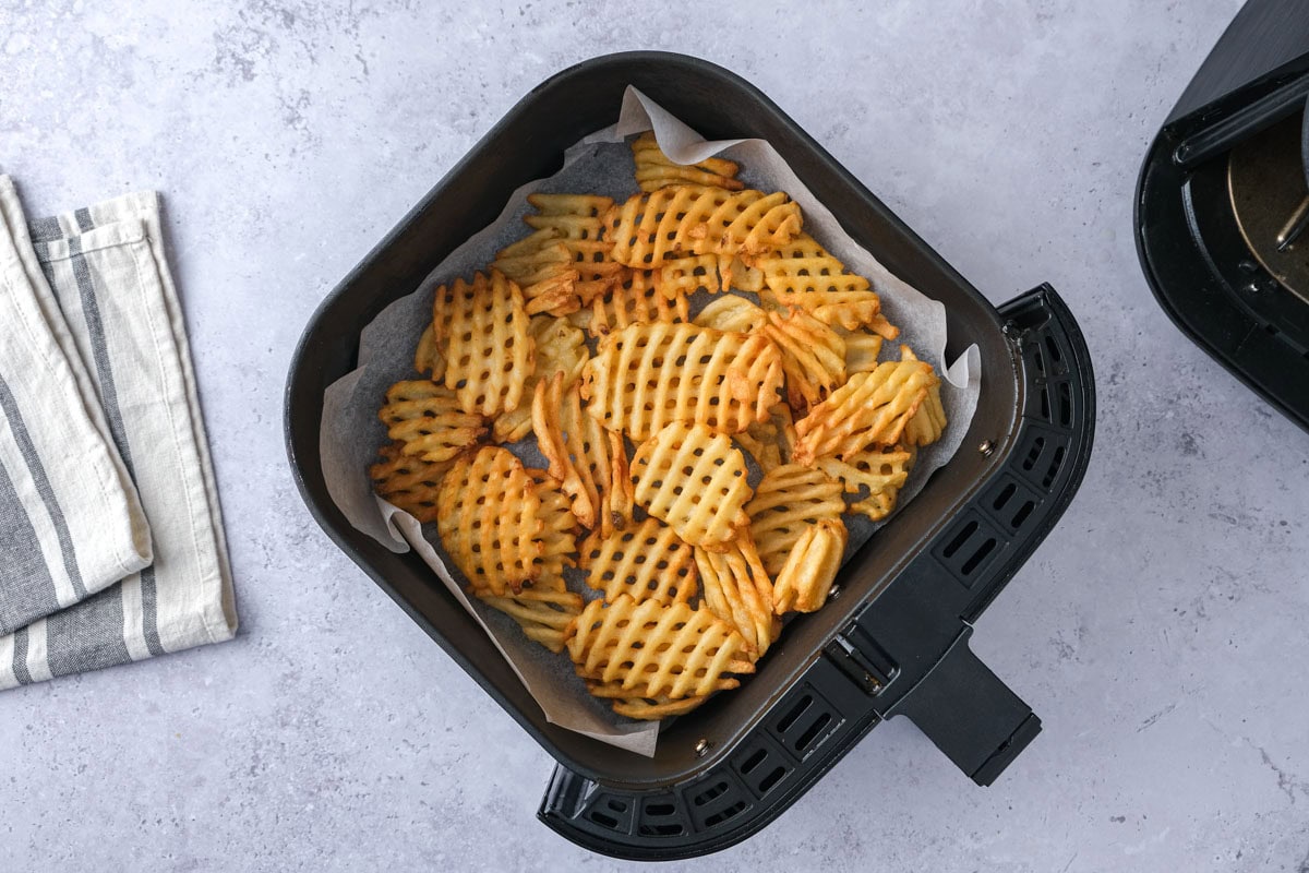 cooked waffles fries in air  fryer basket on trimmed parchment paper.