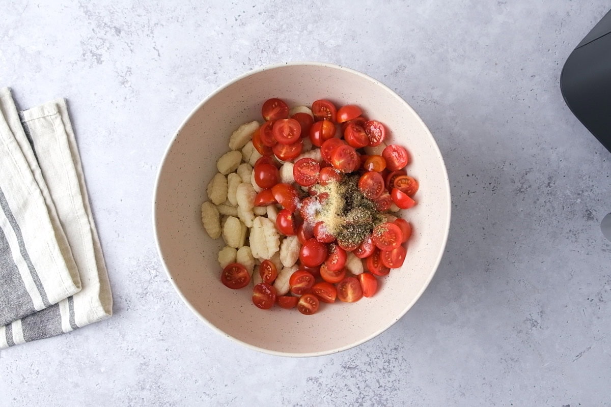 raw cherry tomatoes and gnocchi in a bowl with spices on counter.
