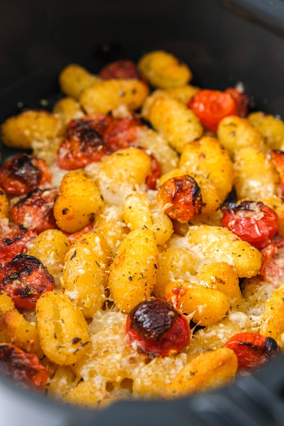 crispy cherry tomatoes and gnocchi in air fryer basket.