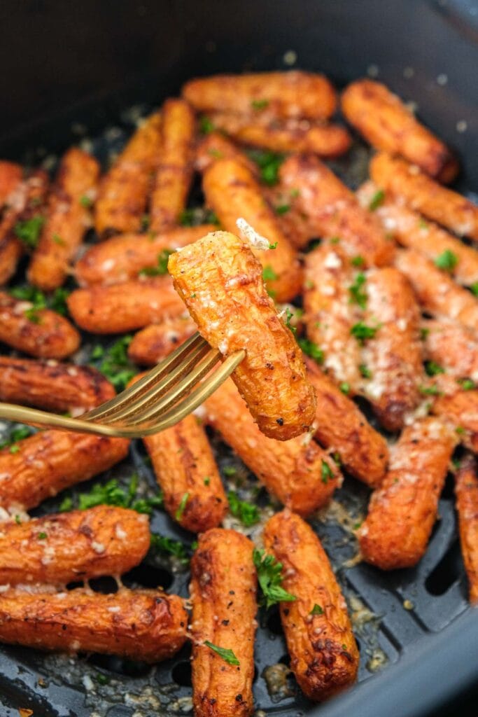 golden fork piercing baby carrot with air fryer basket behind.
