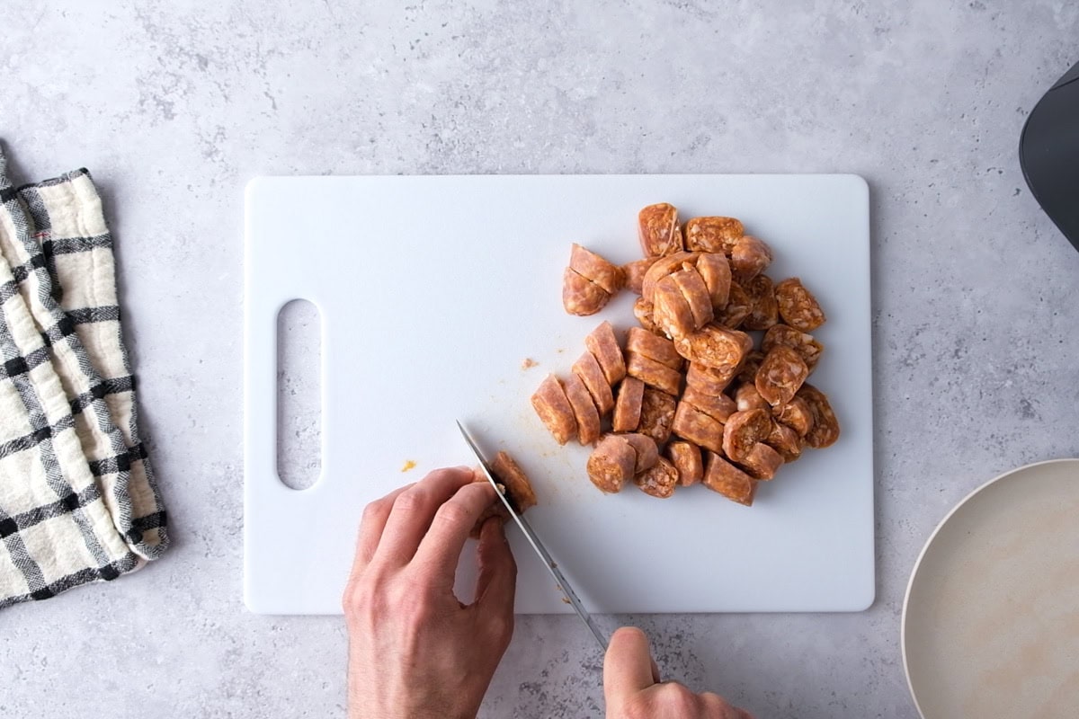 hand cutting raw sausage on white cutting board on counter.