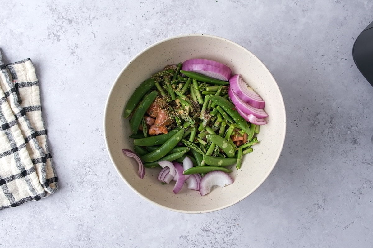 mixing bowl full of green vegetables and raw cut sausage.